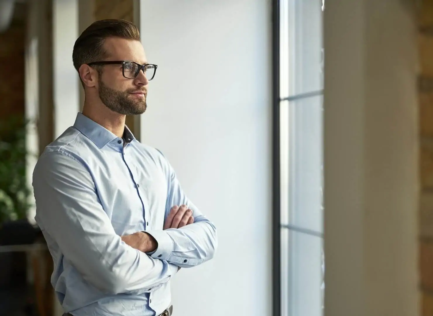 Homem de negócios de braços cruzados olhando estrategicamente pela janela de um escritório. Representa a visão de longo prazo e a busca por liquidez no mercado de capitais através da Value Securitizadora.