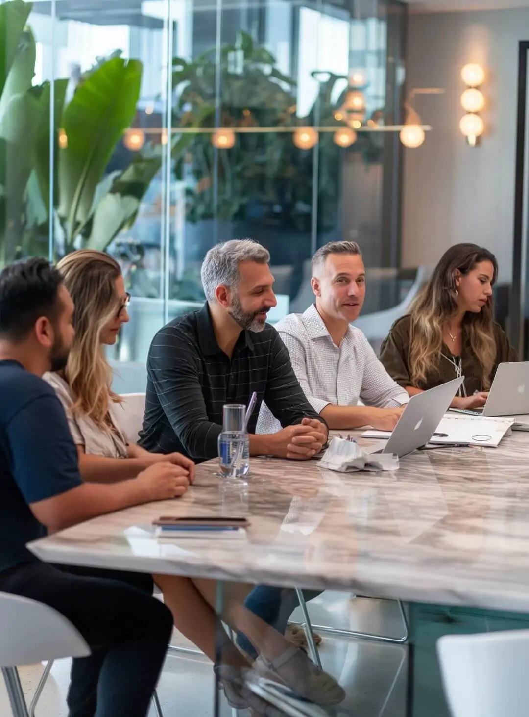 Equipe de especialistas financeiros conversando de forma engajada ao redor de uma mesa de mármore em uma moderna sala de reuniões. Representa a execução técnica e o planejamento em equipe.